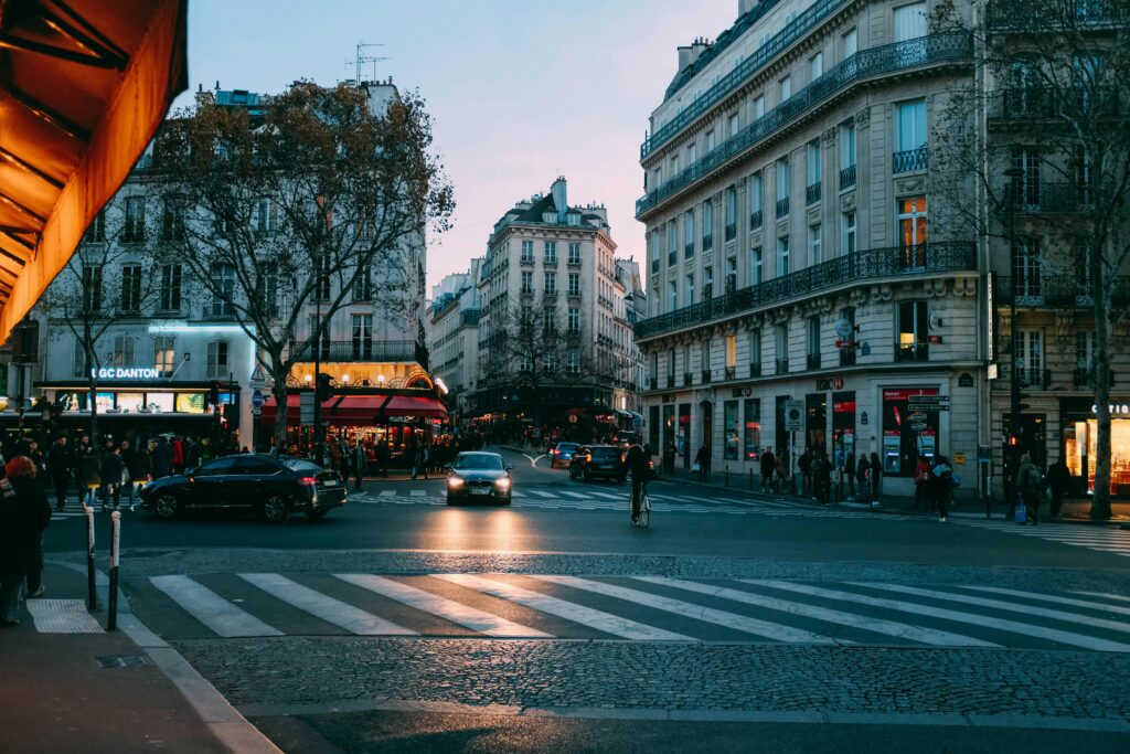 Urban street scene at dusk with cars and pedestrians in a bustling city intersection.
