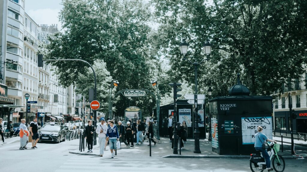 A bustling scene at a Paris metro entrance with people, trees, and signage.